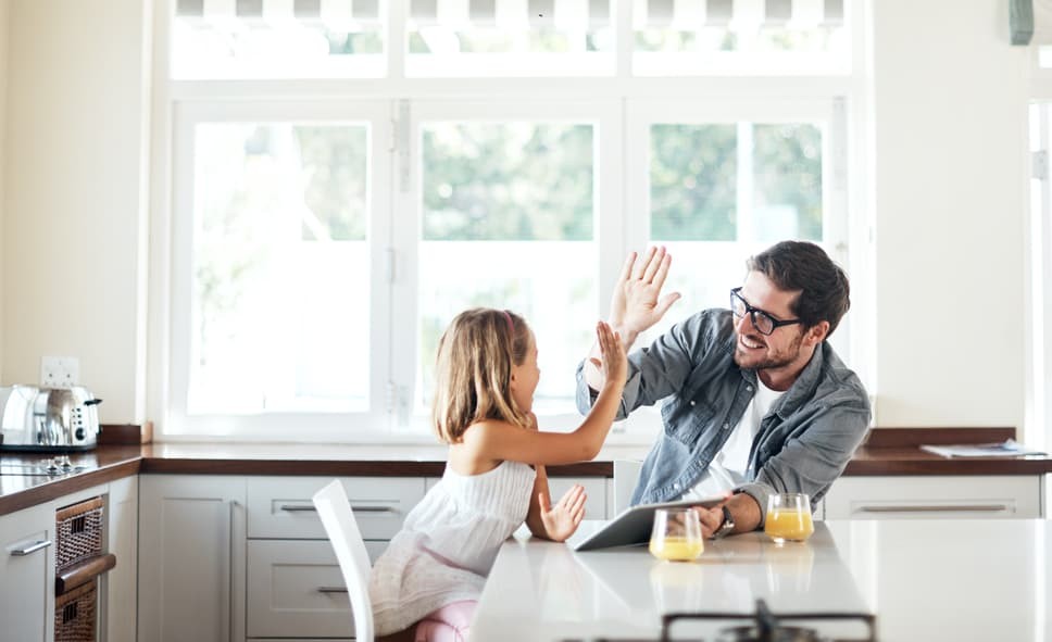 father and daughter high-five in front of white windows in the kitchen