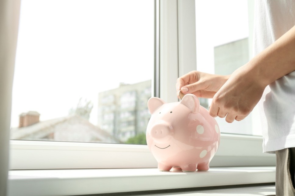 Person putting a coin inside a piggy bank in front of an insulated window